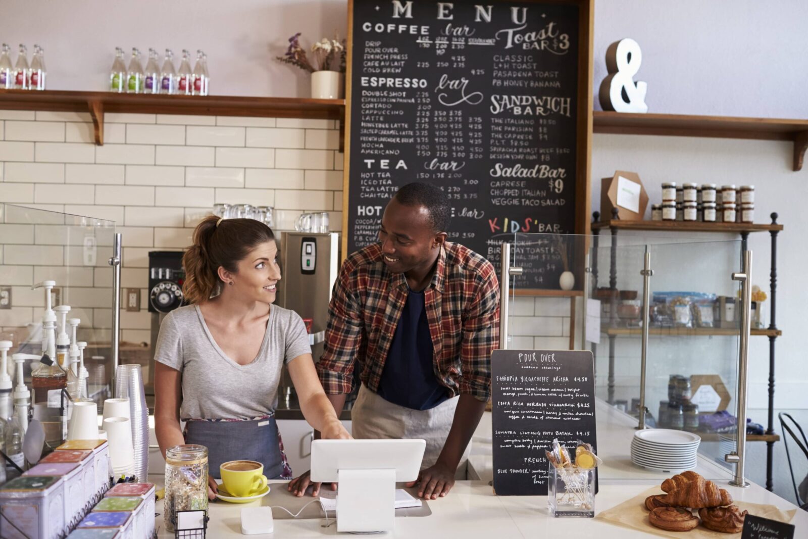 Barista at a coffee shop showing the till to to a new employee during employee onboarding