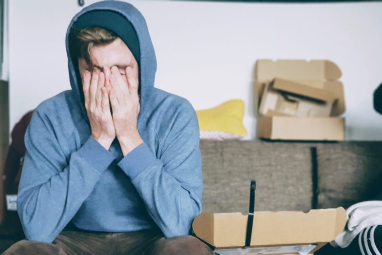 Man in blue hoodie with hands on his face looking stresses