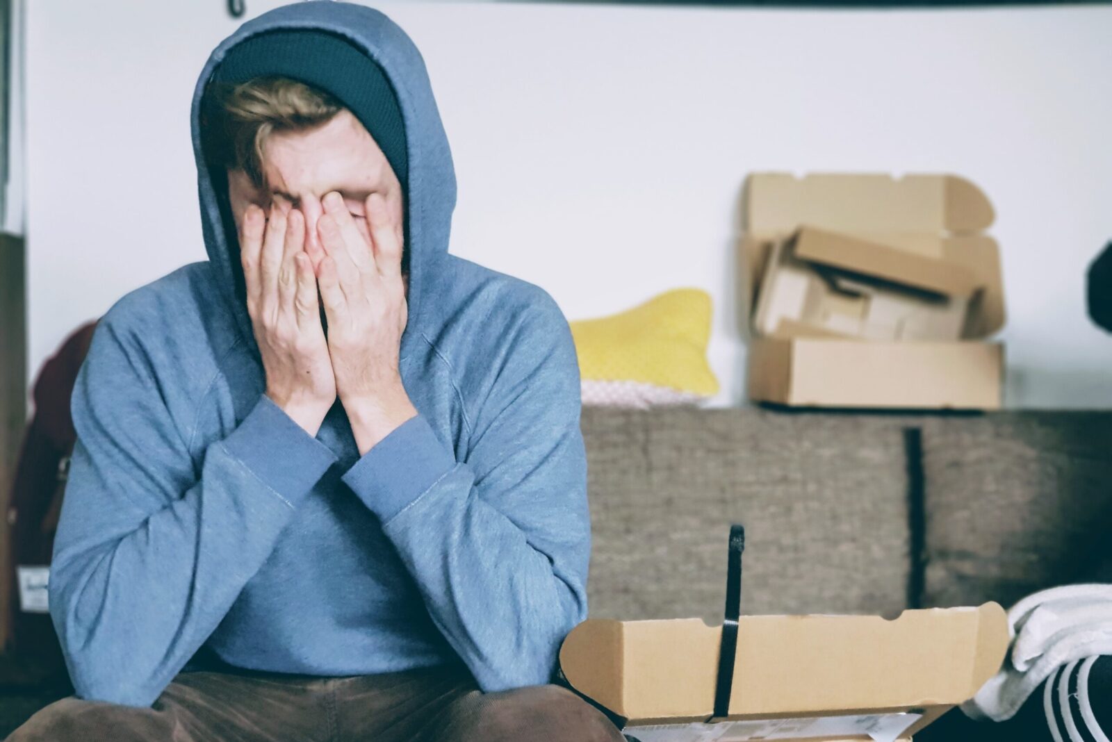 Stressed man in blue hoodie Man in blue hoodie with hands on his face looking stresses