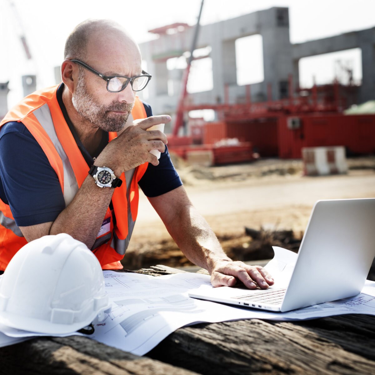 Construction Worker Construction worker drinking coffee and working on his computer on a construction site