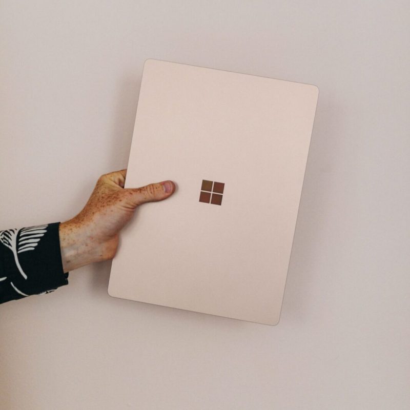 A persons forearm and hand holding a Microsoft Surface laptop