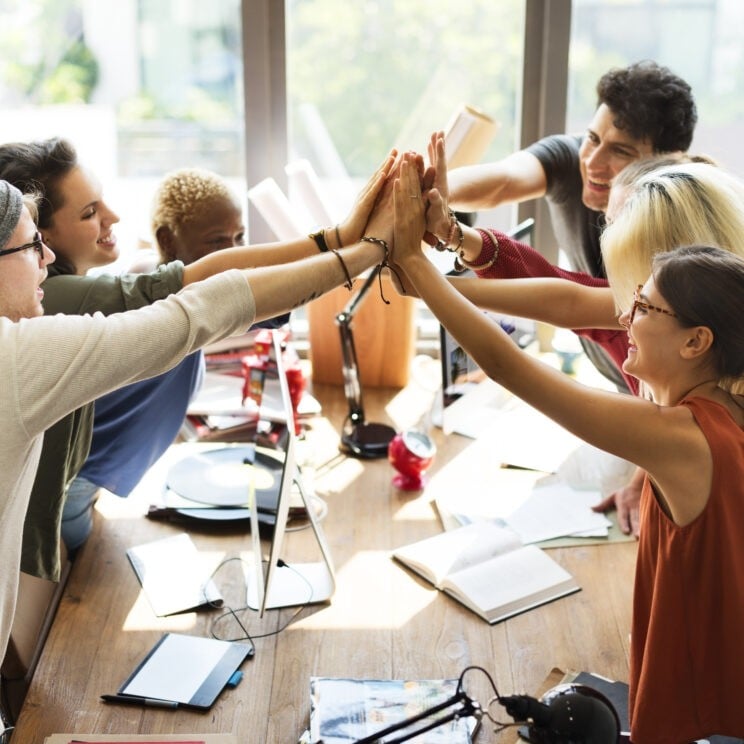 A group of employees all high fiving each other across a desk