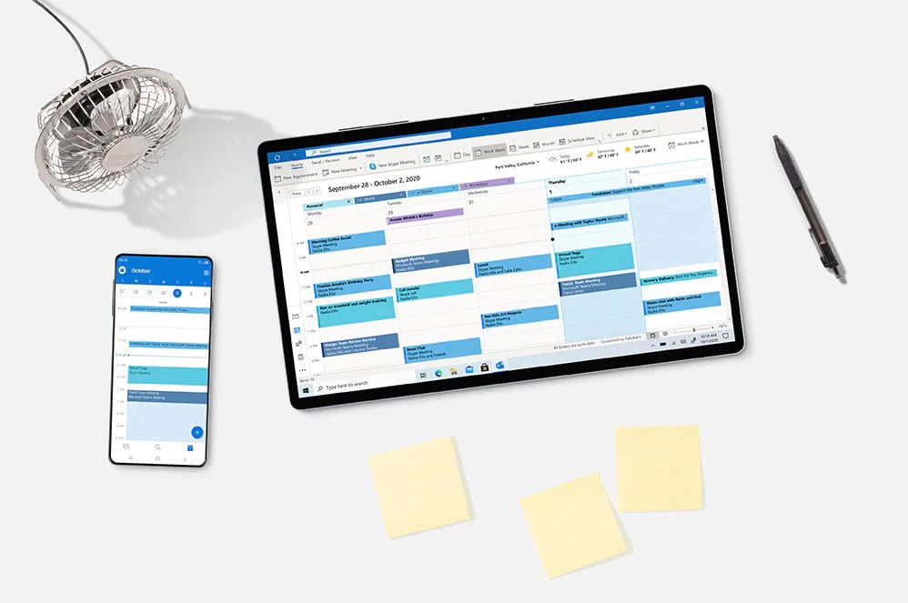 tablet and mobile phone on desk with outlook calendar open with a fan and pen