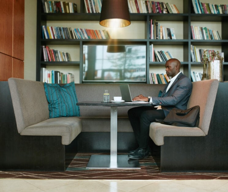 African businessman working on laptop at cafe Man working on a laptop in an office booth with wearing a black and white suit