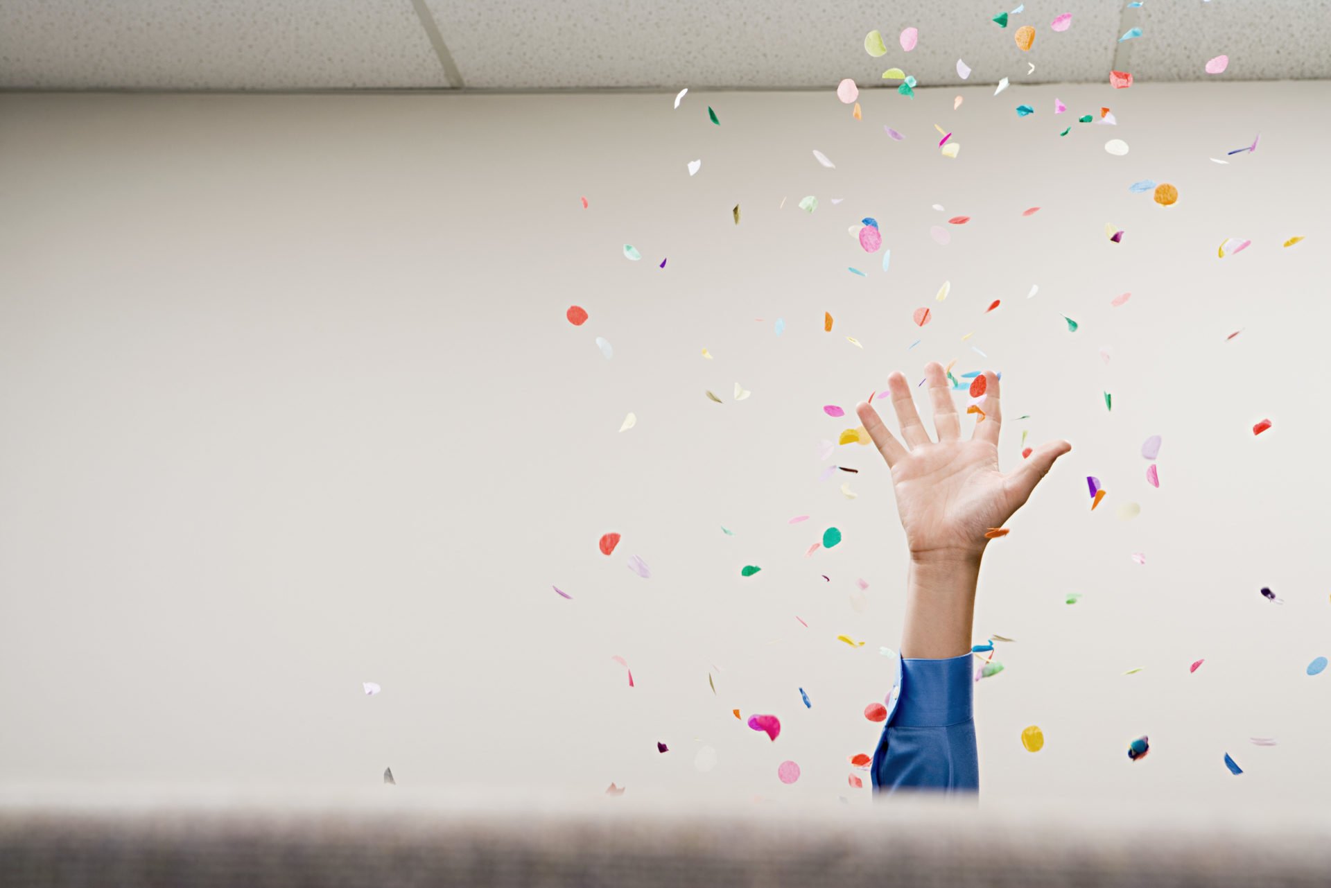 Hand reaching up in celebration and confetti falling from ceiling