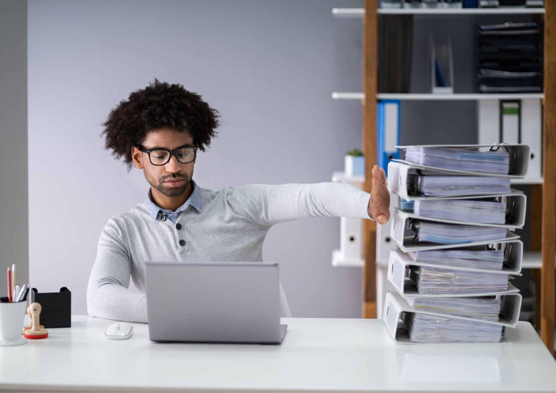 Man looking at his computer and holding his hand up against a stack of ring binders in an office