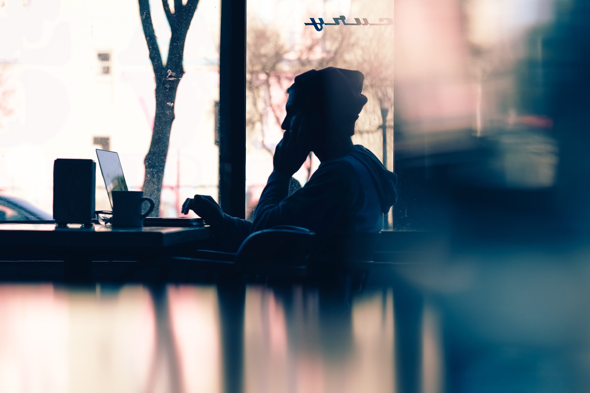 young man talking on a mobile phone and working on a laptop at a table in a coffee shop