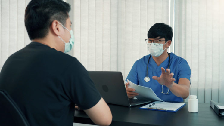 Doctor explaining to patient and reading from paper wearing face masks in an office