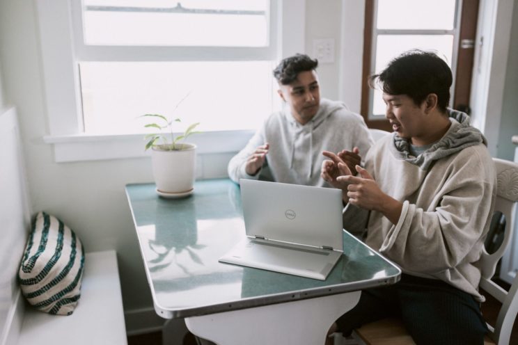 Two young male co-workers talking and gesturing using a laptop