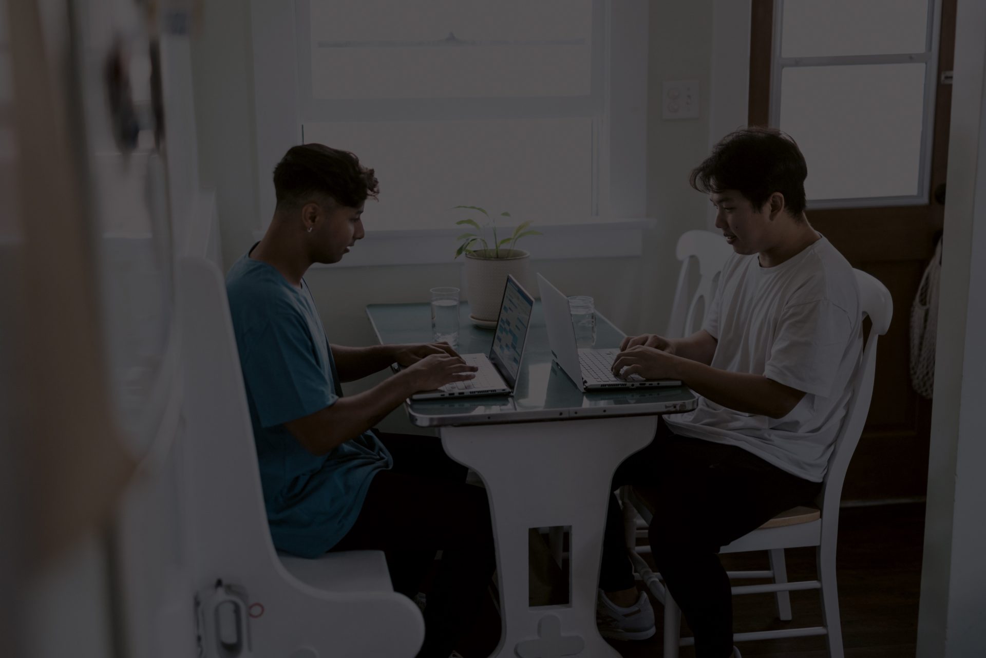 Dark image of Two young male co-workers working collaboratively at home using their laptops