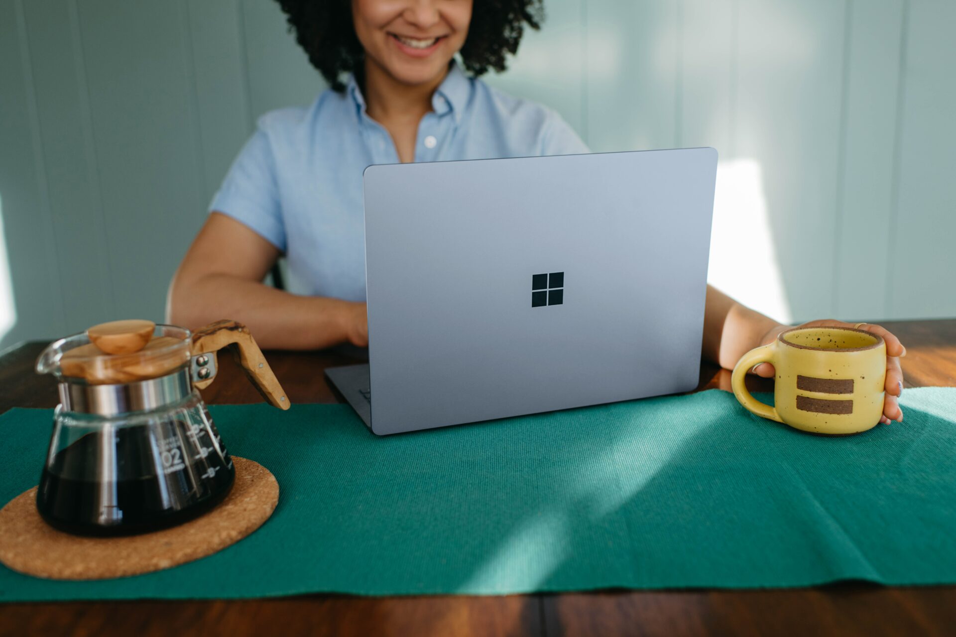 Smiling woman using Microsoft surface laptop holding coffee cup