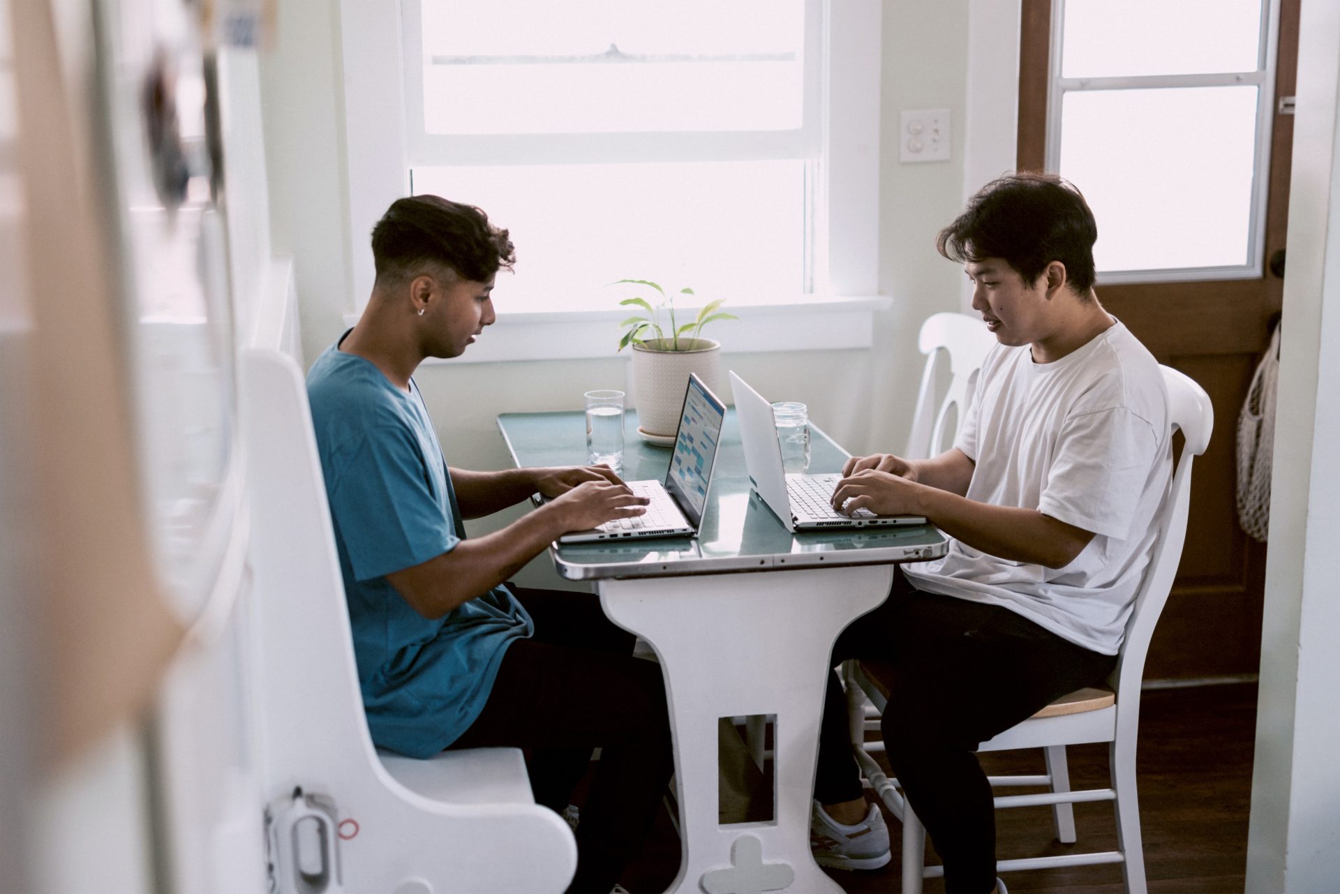 Two young male co-workers working collaboratively at home using their laptops