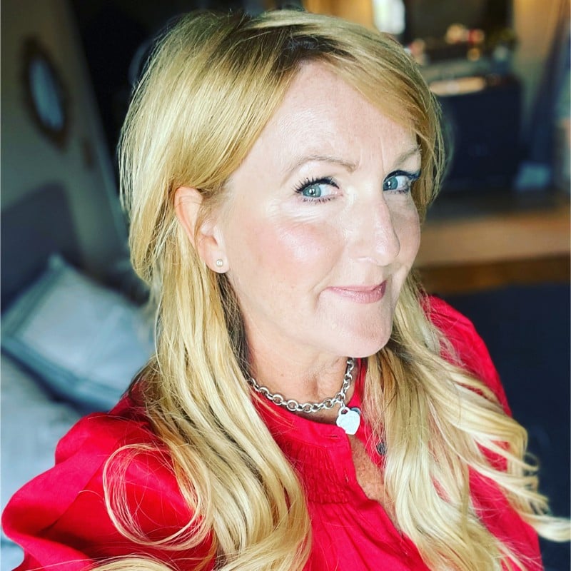 Smiling woman in pink top taking a selfie in her bedroom