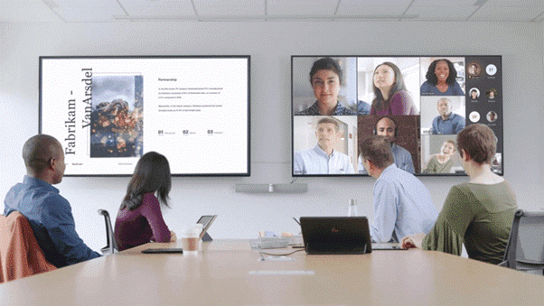 A group of colleagues in a meeting looking at two tv screens