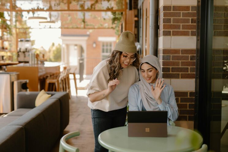 Two Women at a café waving at the screen of a Microsoft surface tablet