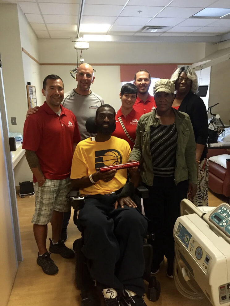 a group of people, one person in a wheelchair, in a hospital room, smiling