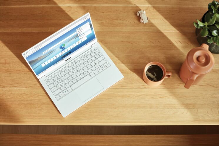 open windows laptop on a wooden table, next to a mug of coffee