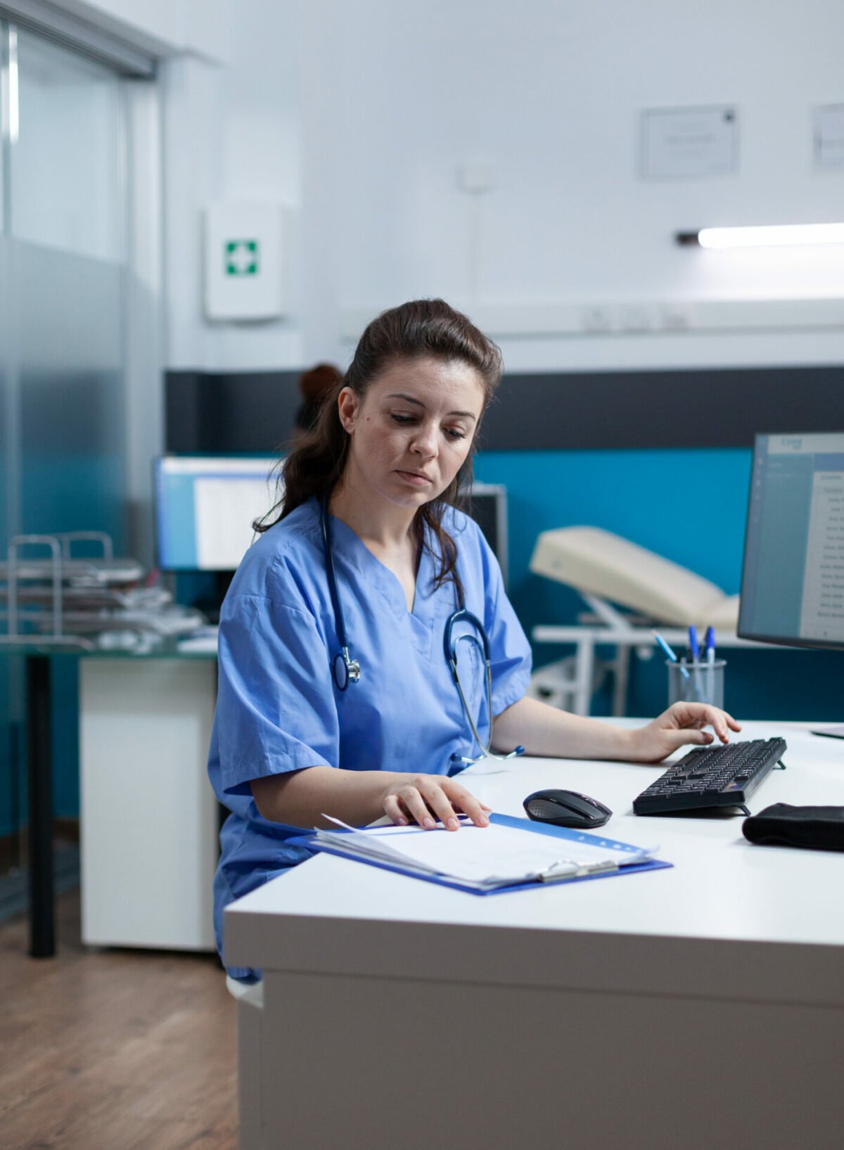 Practitioner nurse with stethoscope analysing healthcare treatment on medical paperwork typing sickness expertise working in hospital examination office. Woman assistance checking disease results