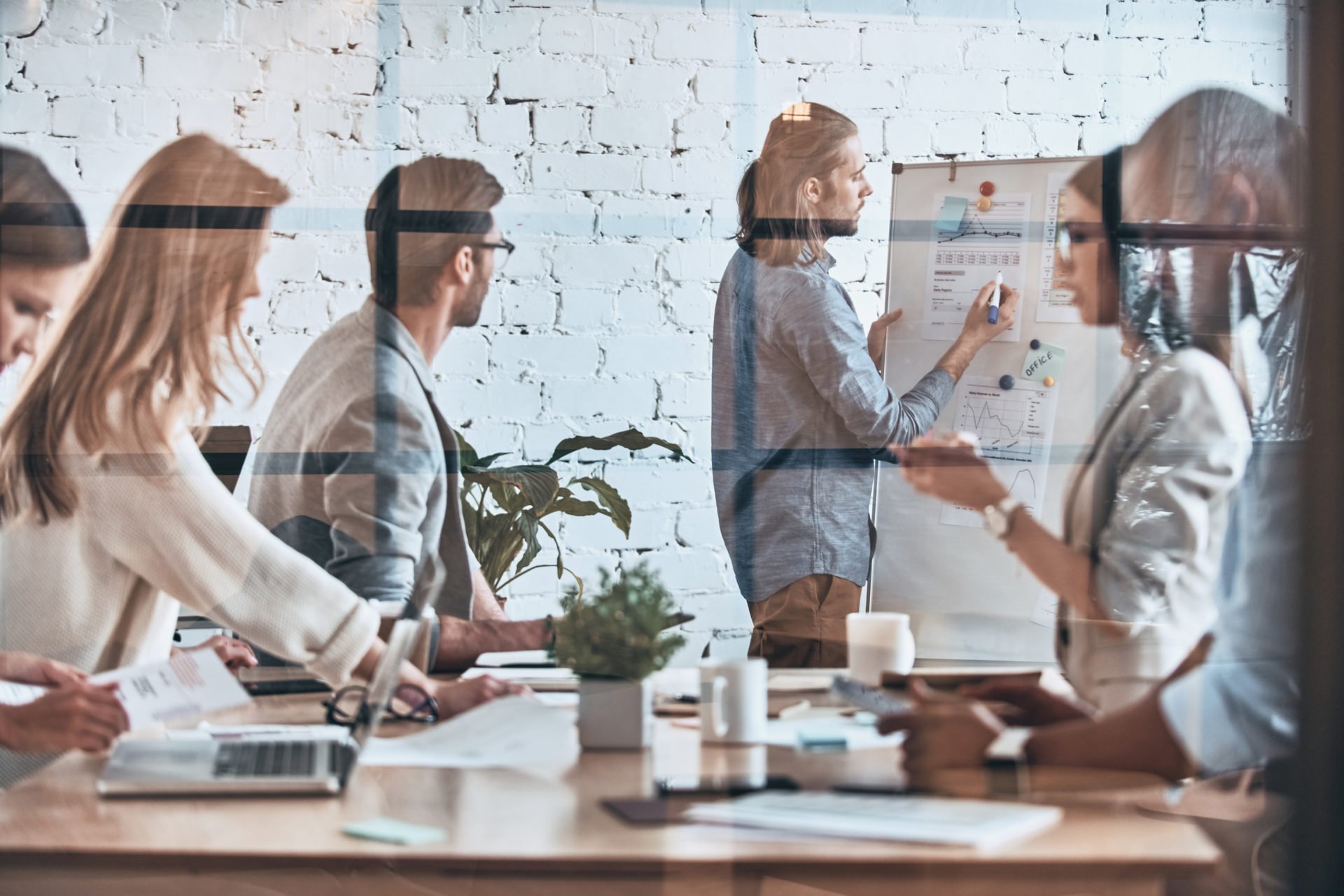 Man presenting ideas on a whiteboard to a team listening and working on laptops in a meeting room