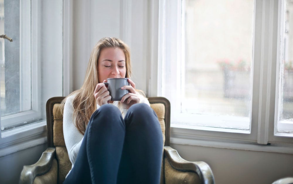 Happy woman sat on a cosy chair drinking out of a mug