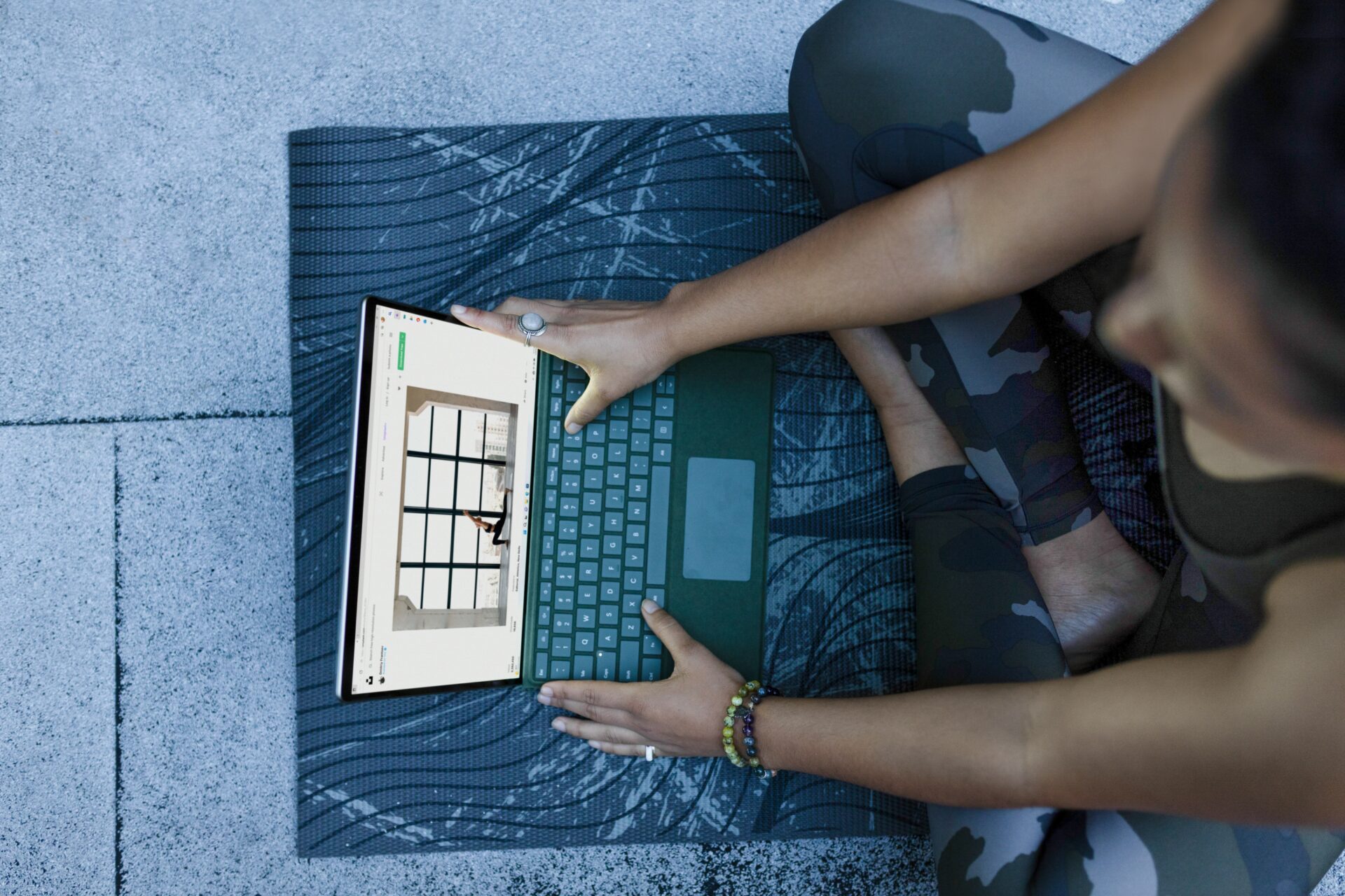 A woman sits cross-legged on a yoga mat, watching a yoga video on her windows laptop
