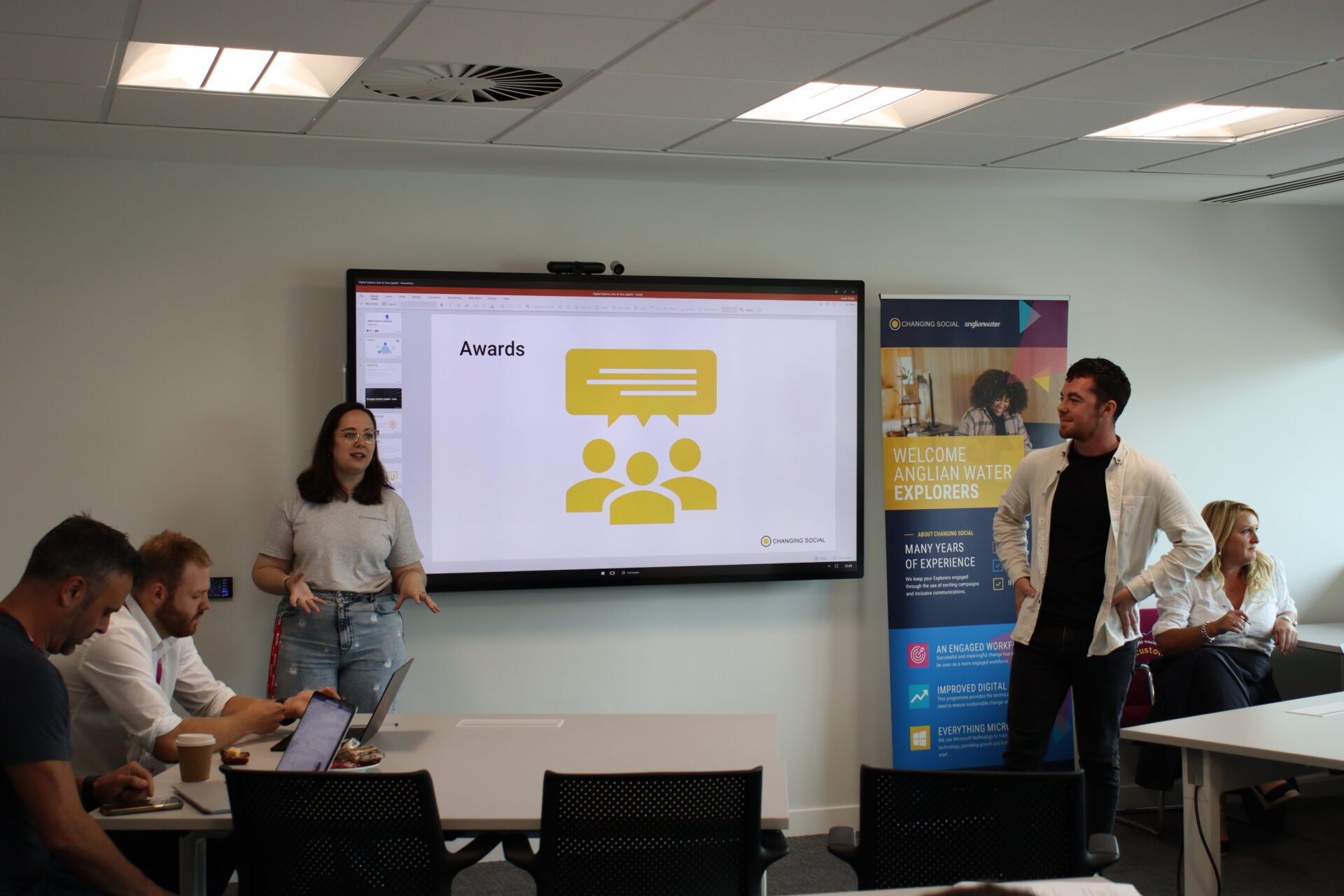 an image of two people at the front of the room, standing either side of a whiteboard. they appear to be presenting to a room of people