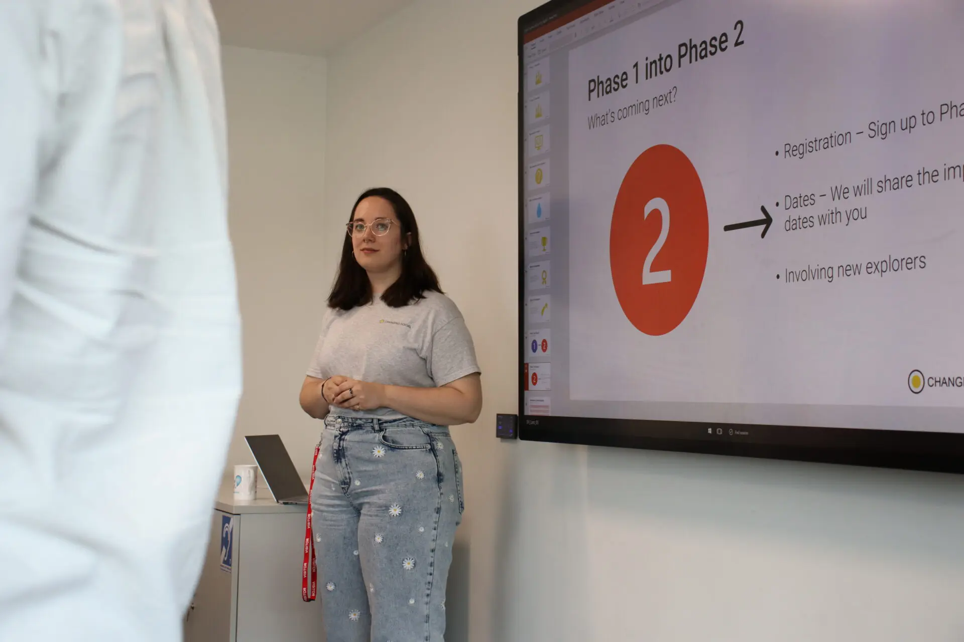 an image of a person wearing jeans and a t-shirt, standing by an electronic whiteboard.