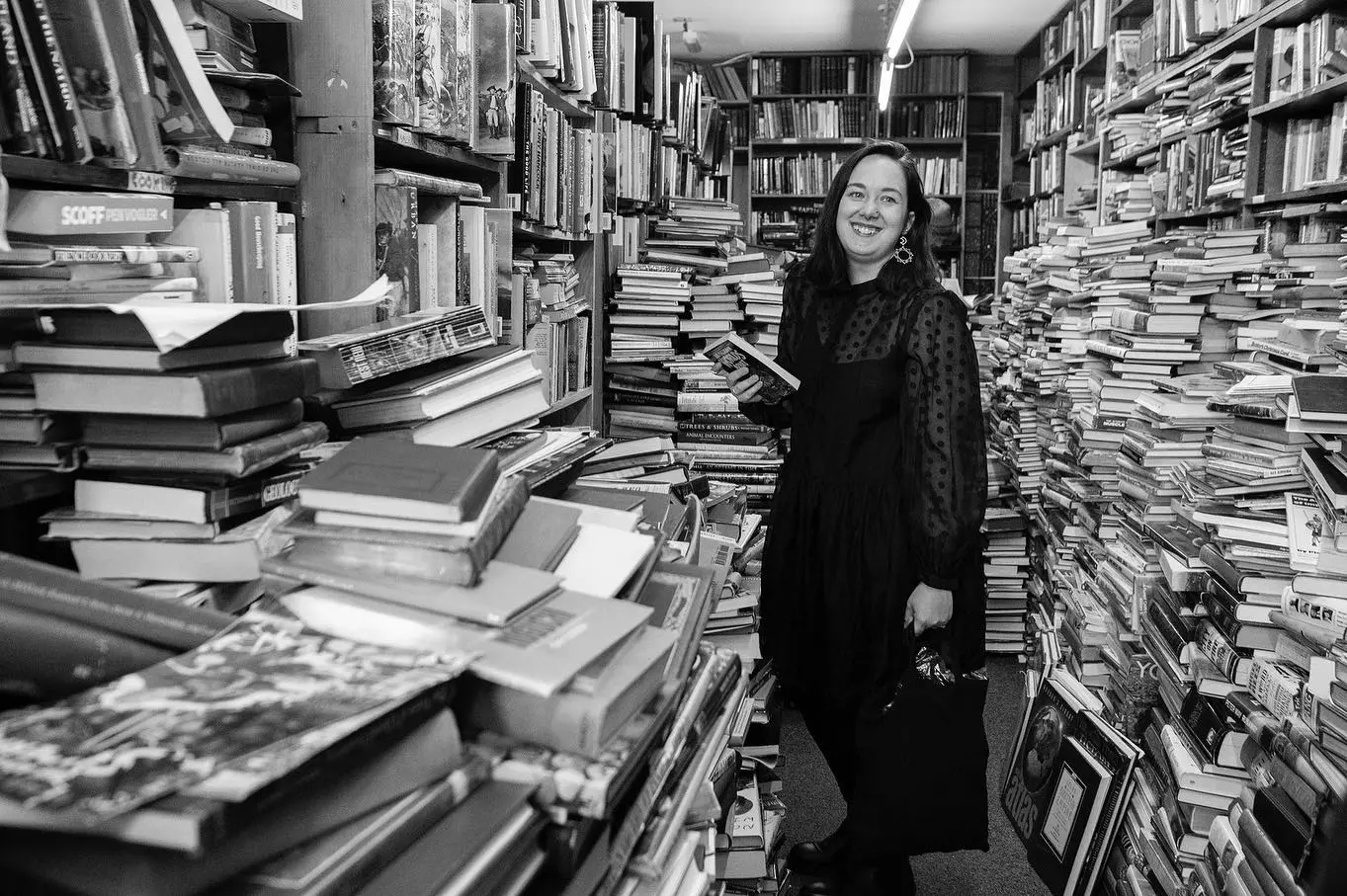 a black and white image of a person standing and smiling, surrounded by books