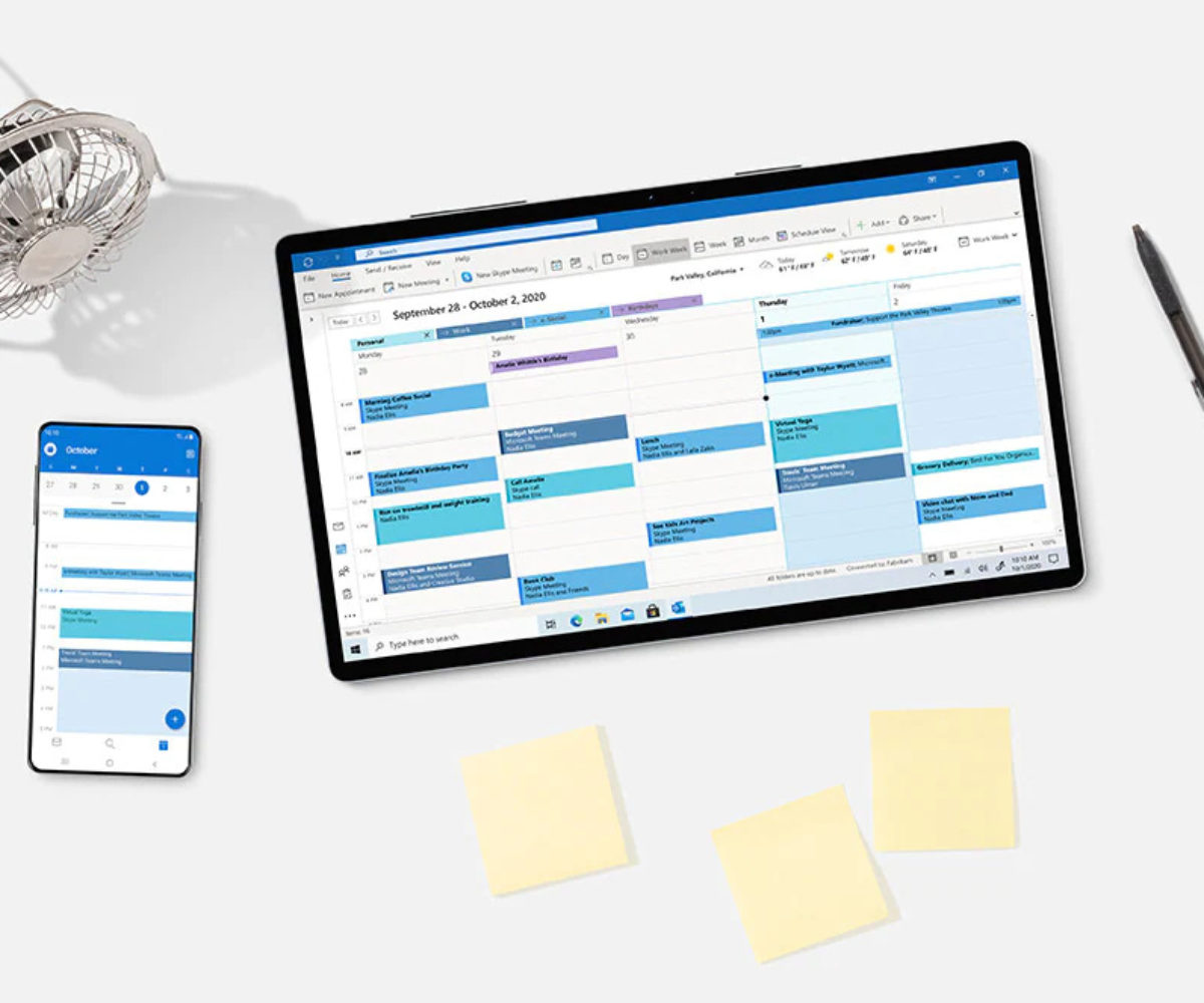 tablet and mobile phone on desk with outlook calendar open with a fan and pen